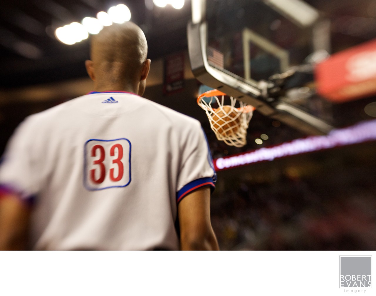 A player wearing number 33 is photographed from behind facing a basketball hoop.