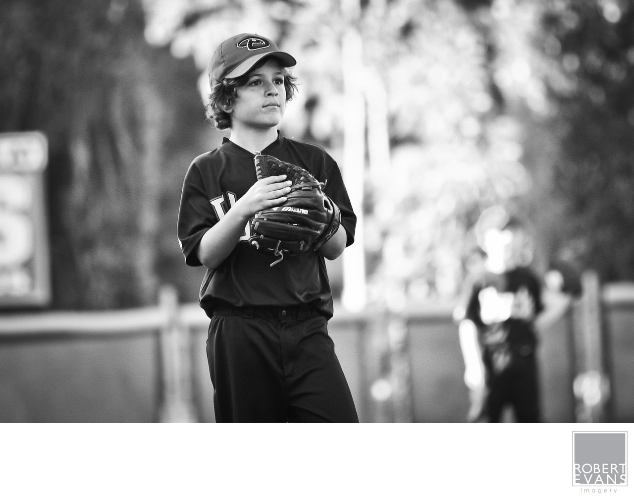 A youth baseball player holds his glove and looks upward in black and white.