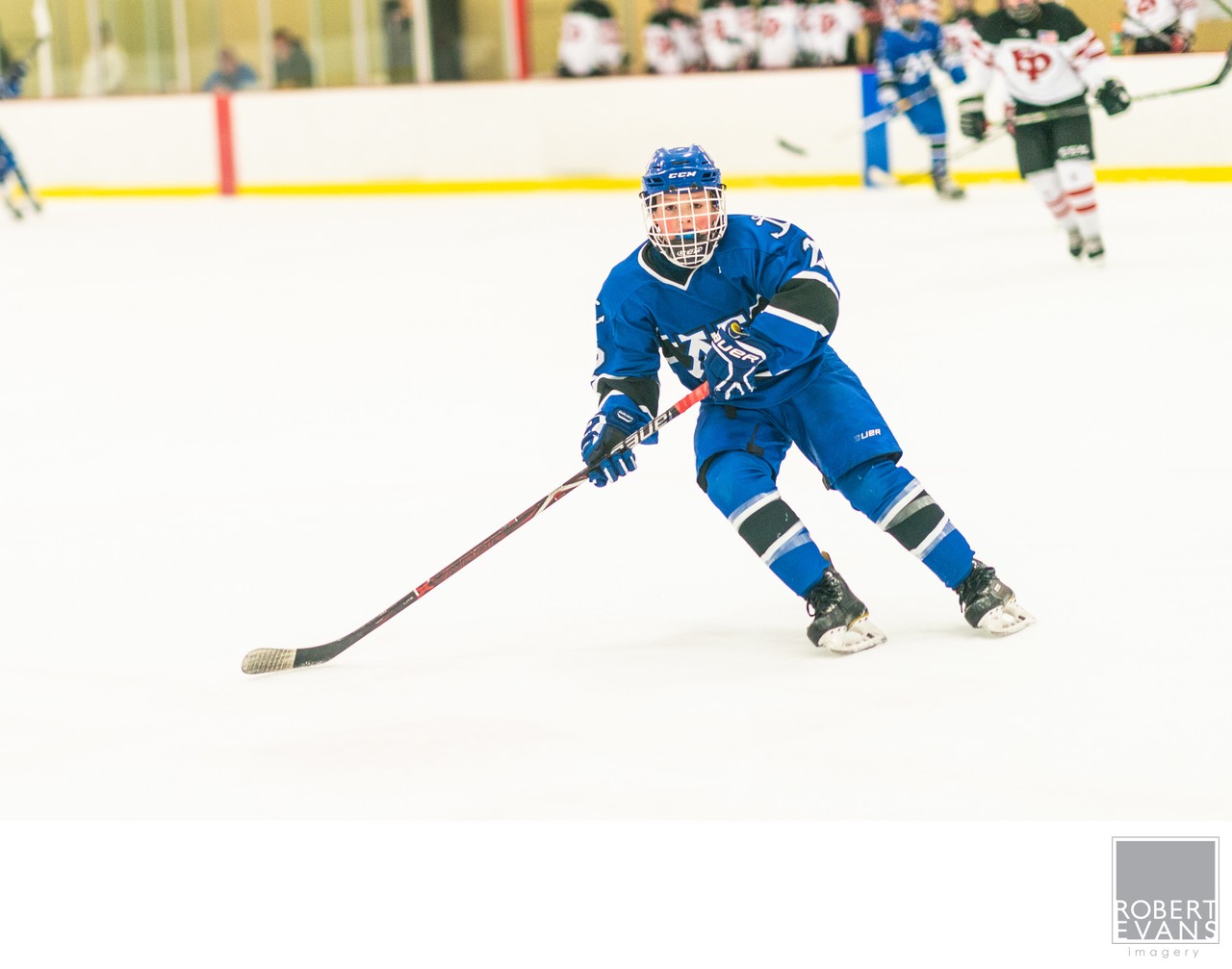 A blue-uniformed player leans into a turn with his stick extended along the ice.