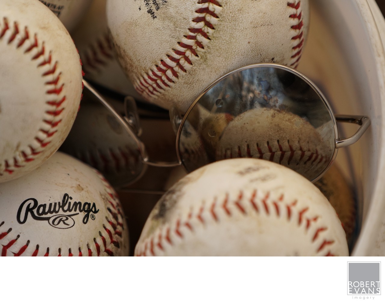 Baseballs surround a pair of reflective sunglasses in a close still-life photograph.