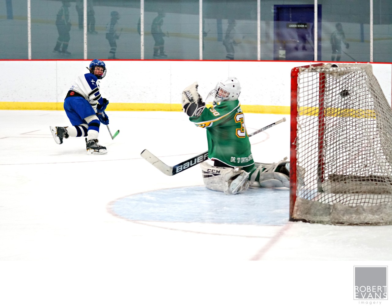 A green-uniformed goalie lifts his glove as an opponent approaches beside the net.