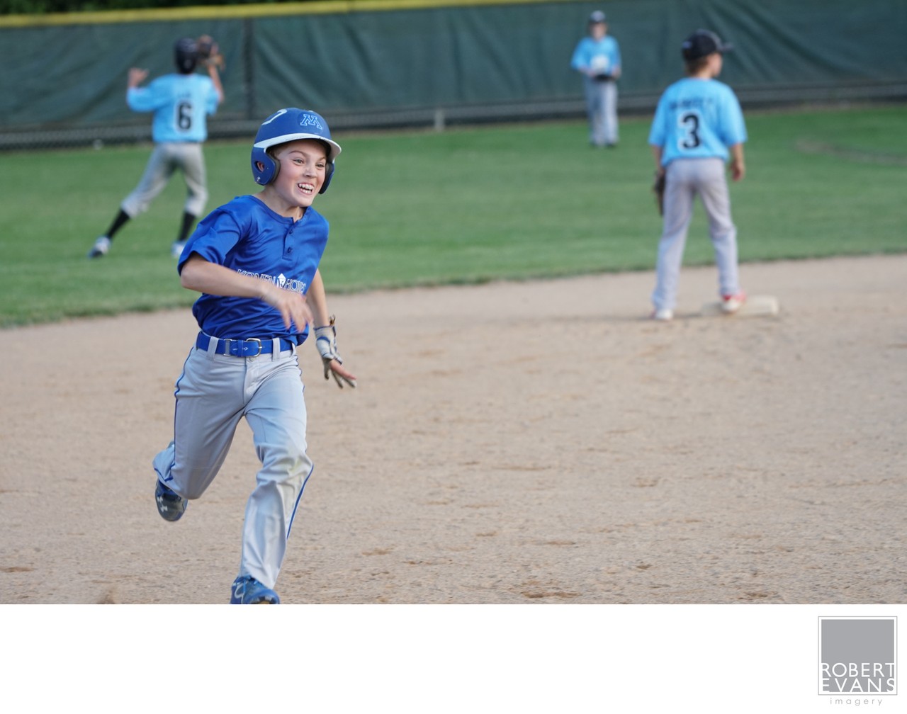A young player in blue smiles while running across the infield.