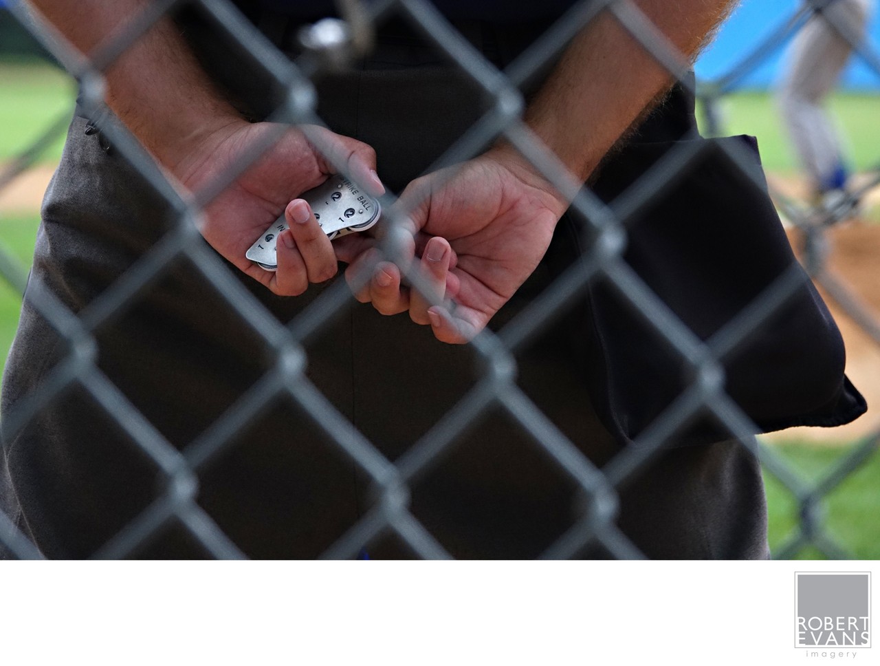 Hands hold a small metal object behind the diamond pattern of a chain-link fence.