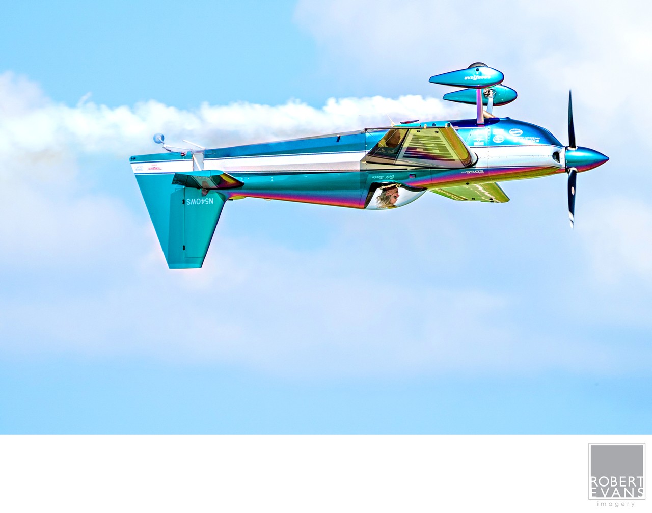 A brightly painted propeller airplane banks against blue sky and white clouds.