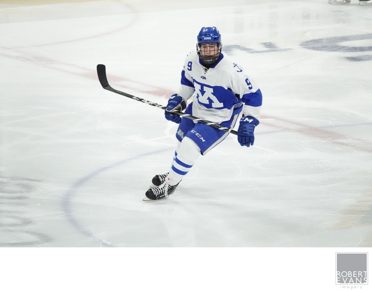 A hockey player in a white and blue uniform skates with his stick extended.