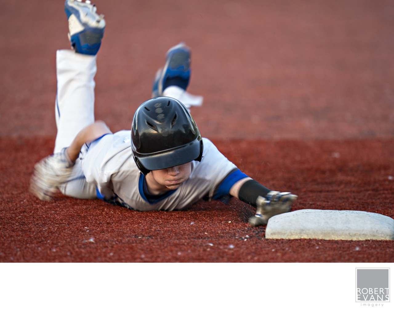 A baseball runner stretches toward the base during a headfirst slide.