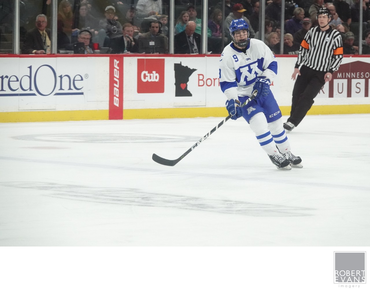 A white-and-blue hockey player skates forward beside an official.