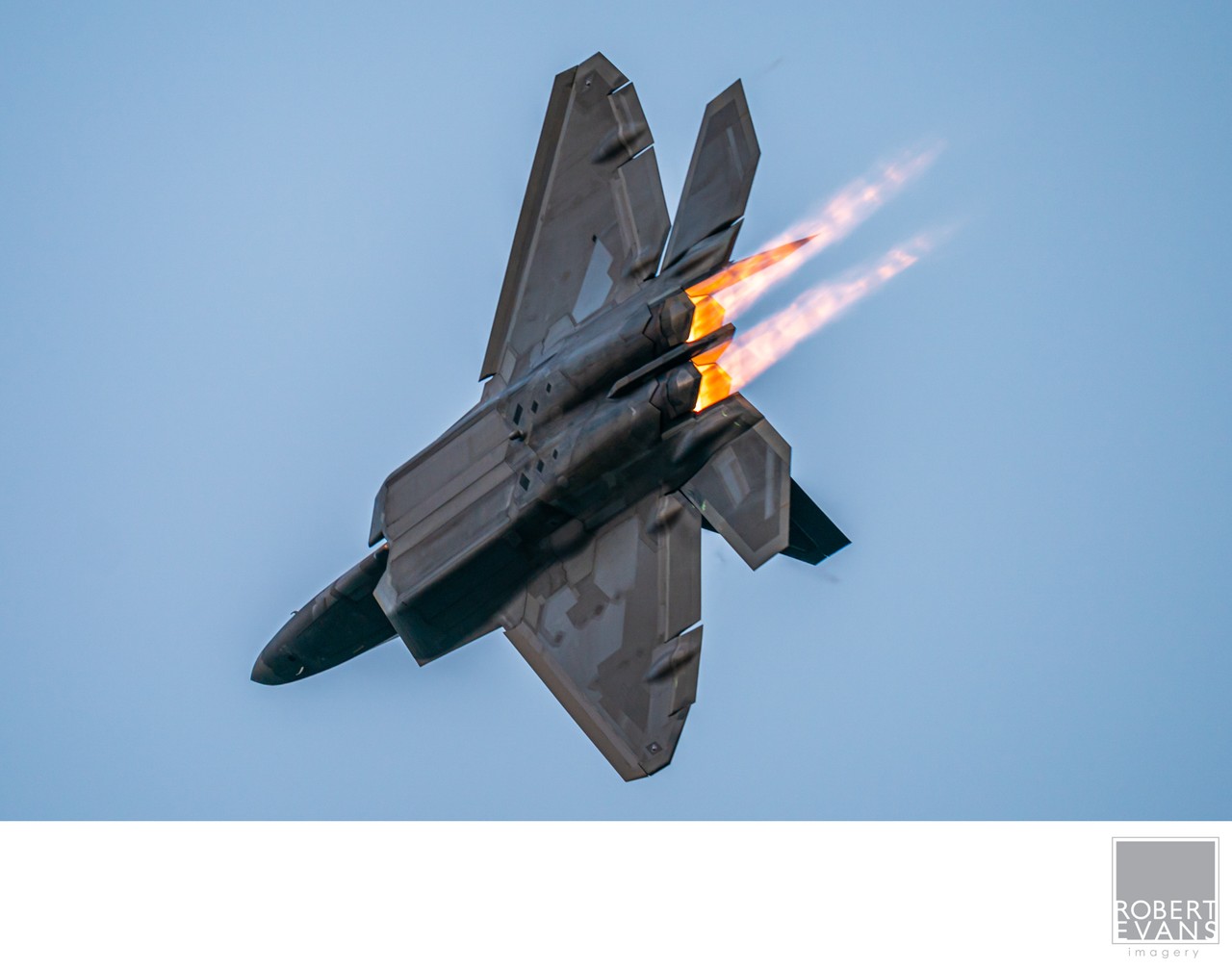 A jet fighter banks sharply against the sky with glowing afterburners.