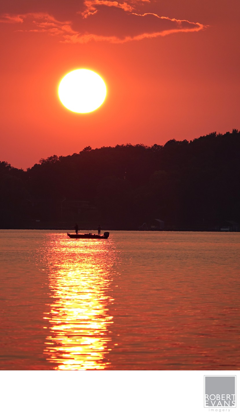 A small boat is silhouetted on water beneath a vivid orange sunset.