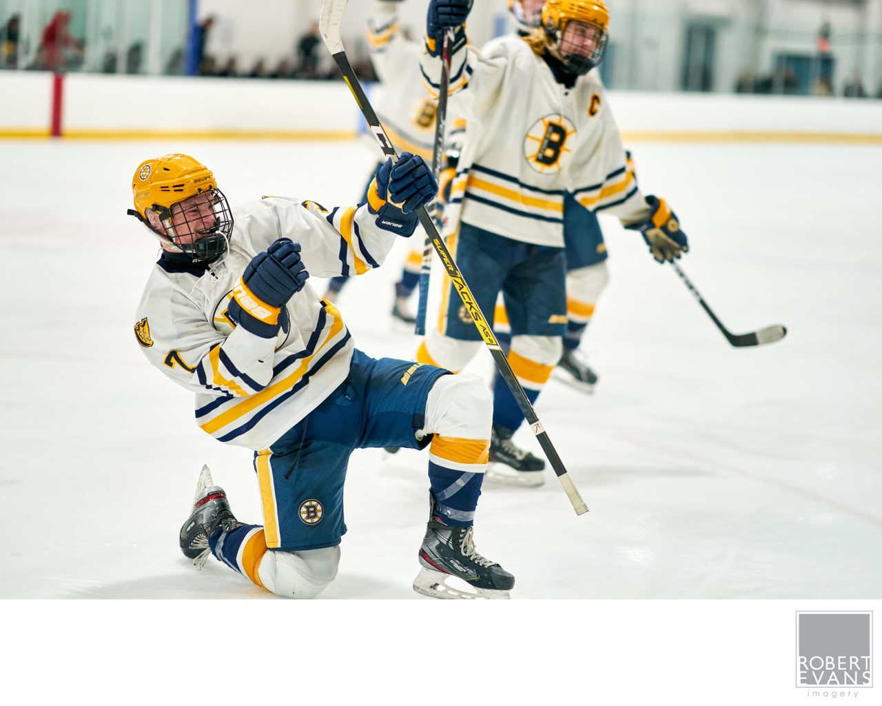 White-and-yellow hockey players celebrate on the ice with sticks raised.