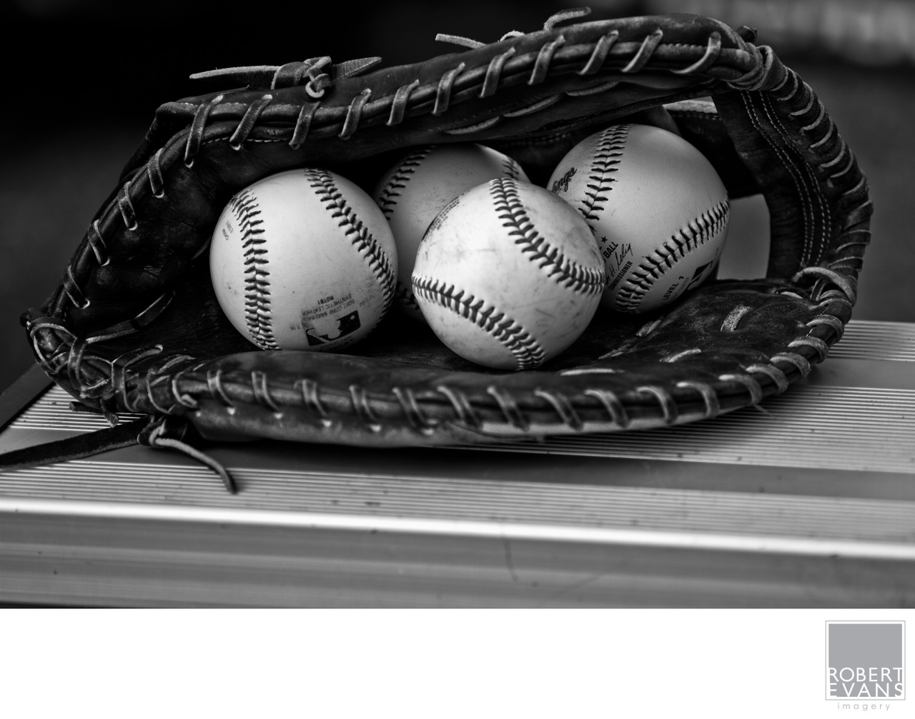 Three baseballs sit inside a leather glove in a close black-and-white still life.