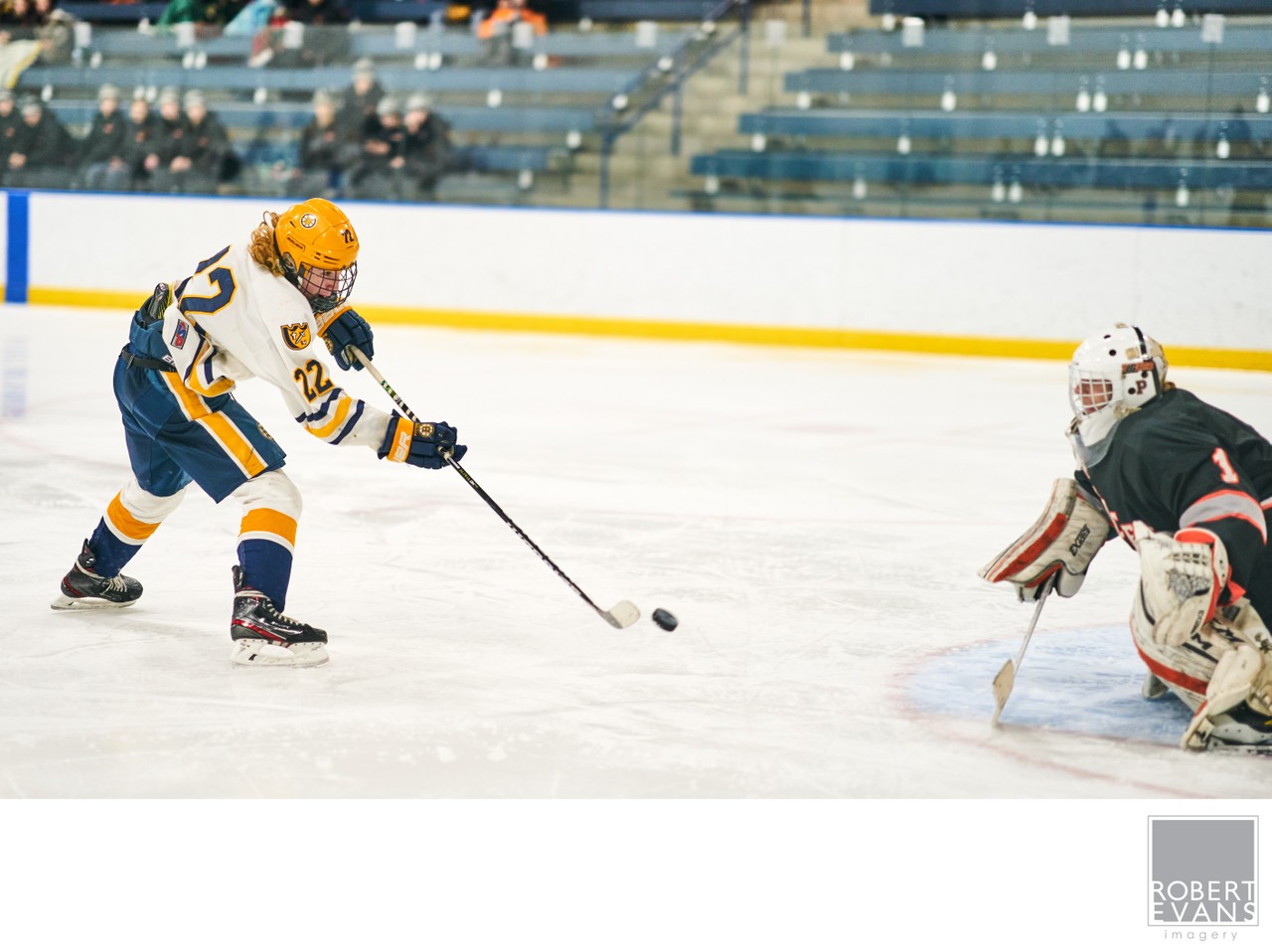 A white-and-yellow attacker directs the puck toward a goalie from close range.