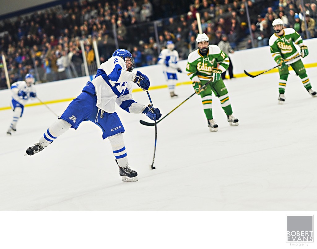 A white-and-blue player follows through on a shot as green-uniformed opponents watch.