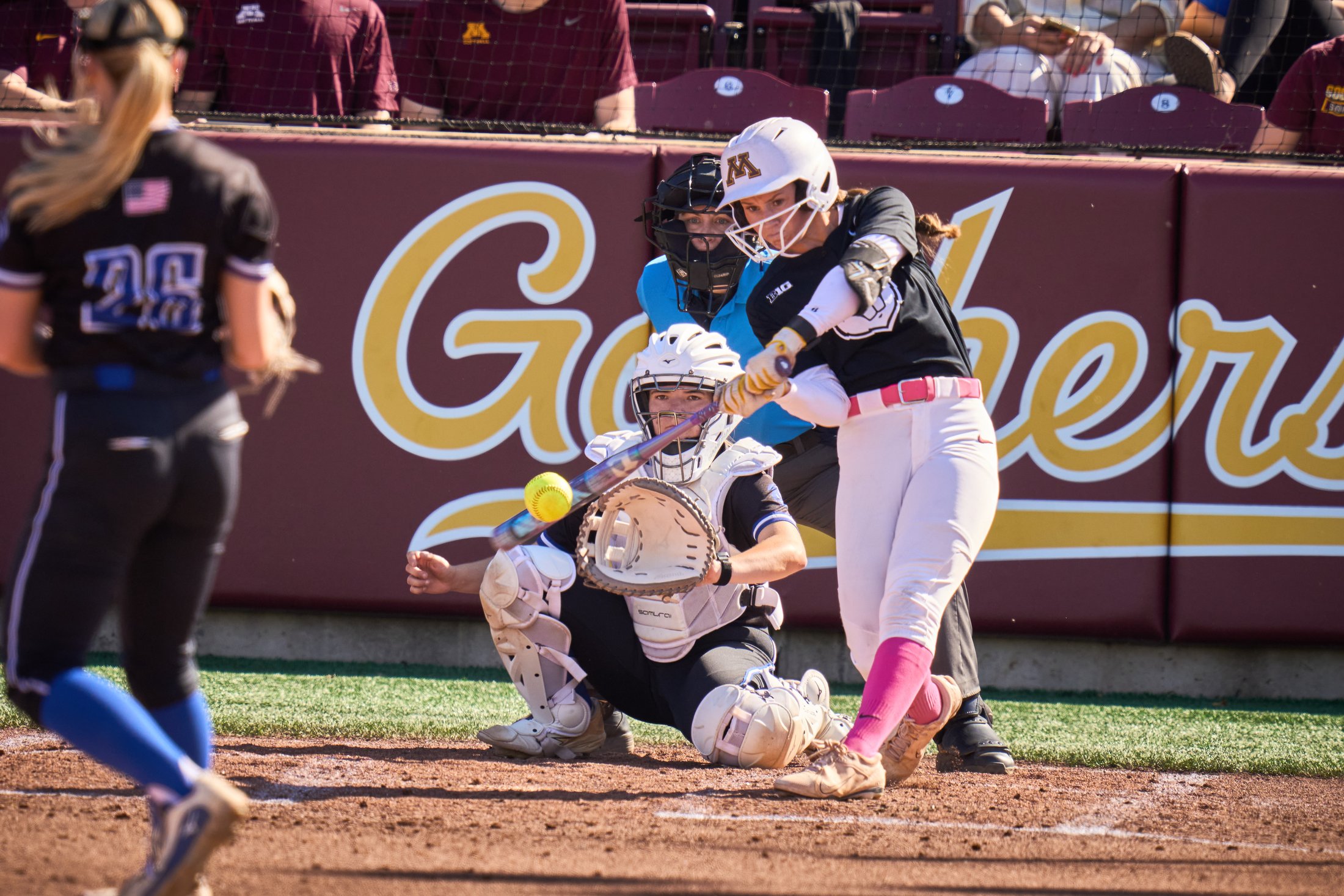 A Minnesota softball batter meets the pitch with the catcher and umpire behind the plate during a fall game against North Iowa Area CC on October 10, 2026.