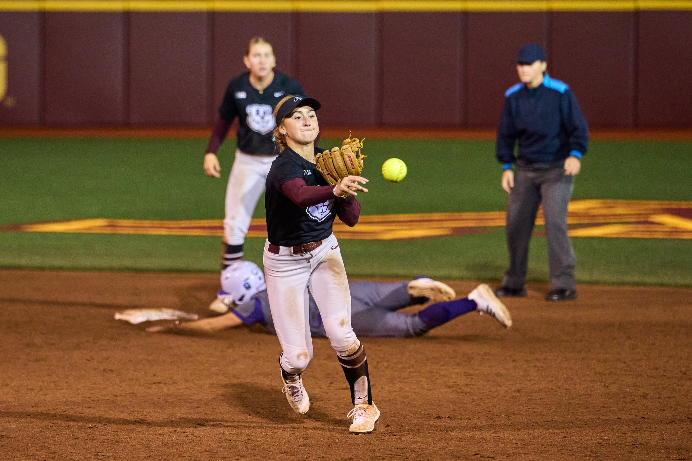 A Minnesota softball infielder releases a throw as an opposing runner slides behind her during a fall game against Winona on October 2, 2026.