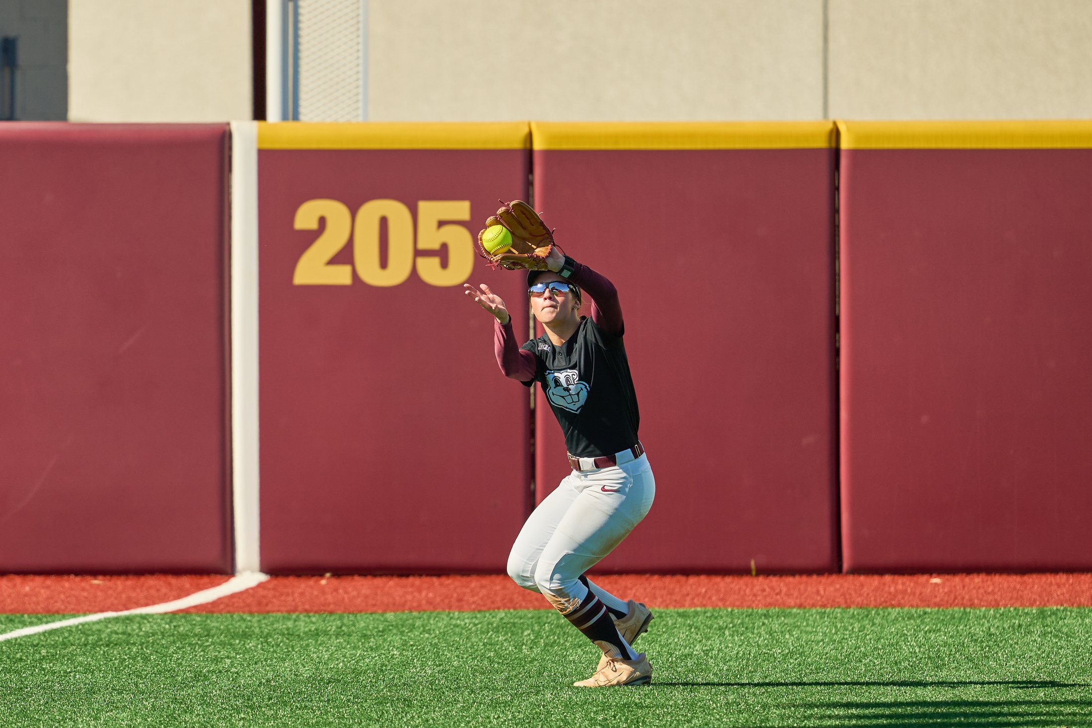 A Minnesota softball outfielder reaches up with her glove near the outfield wall during a fall game against Iowa State on October 4, 2026.