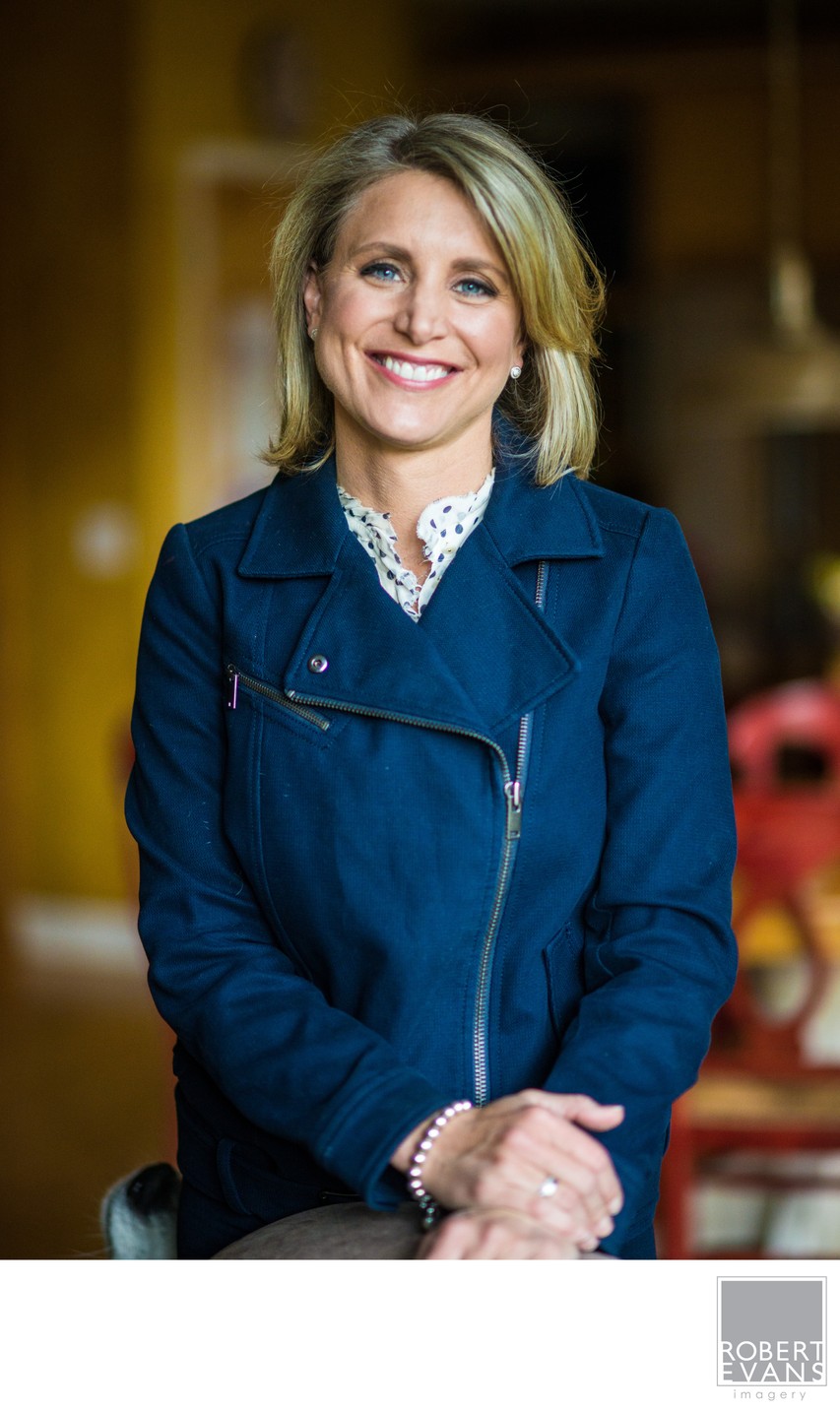 A smiling woman in a blue coat poses indoors against a softly blurred background.