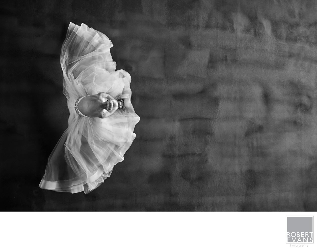 Wedding rings rest on folded white tulle against a textured dark surface in black and white.