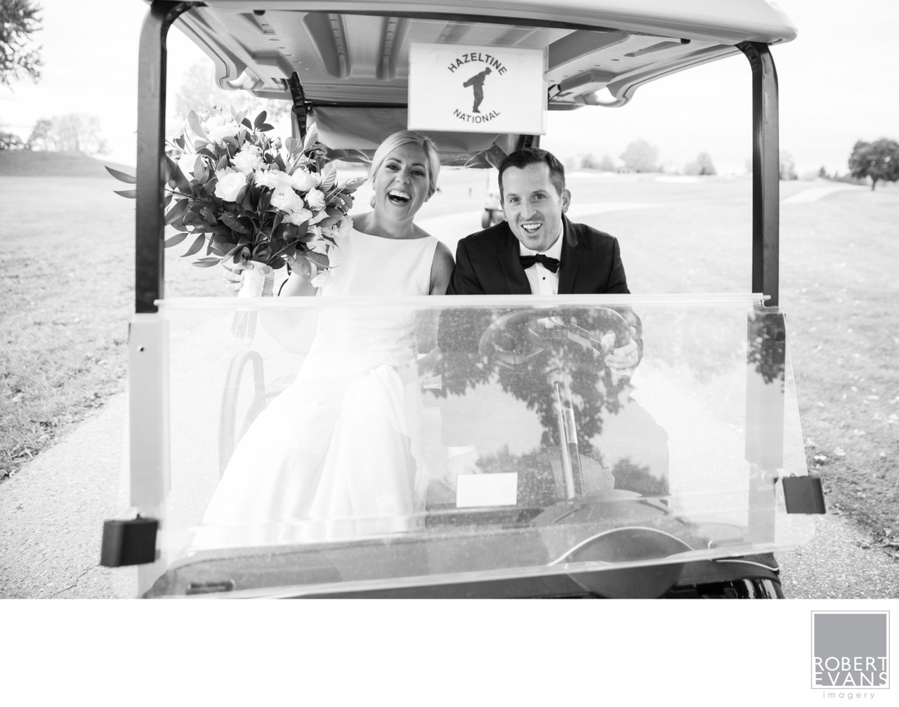 A smiling bride and groom ride together in a golf cart in black and white.