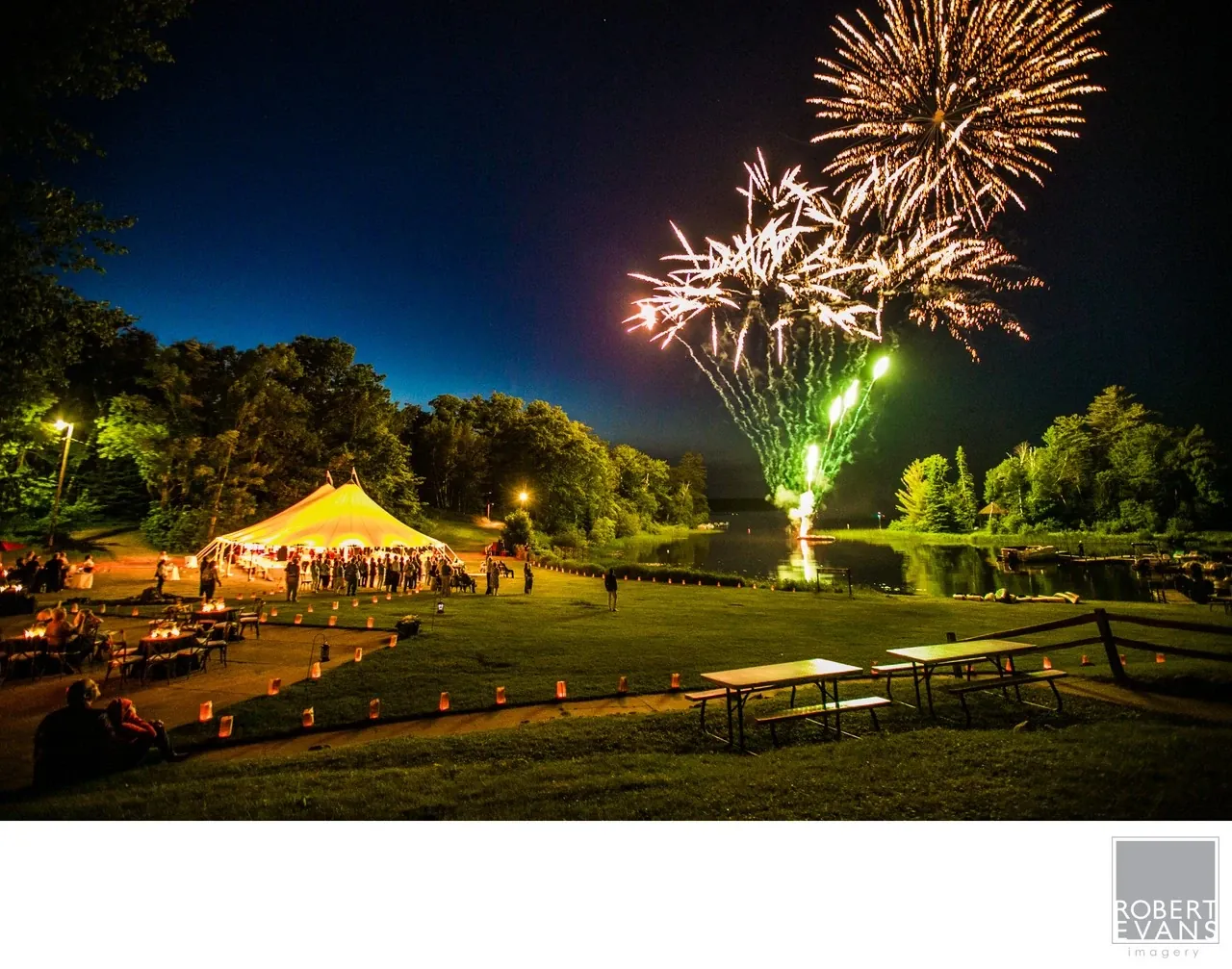 Fireworks illuminate the night sky above a tented outdoor wedding reception.