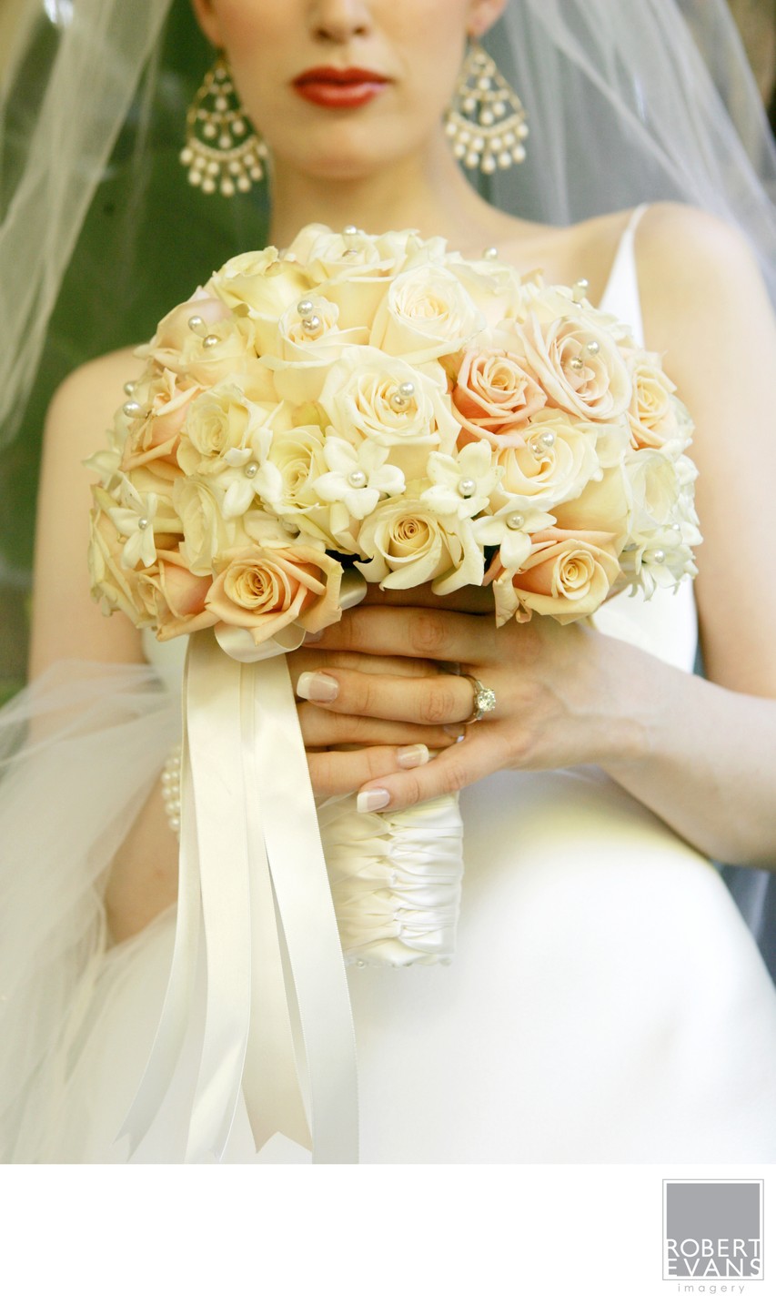 A bride holds a rounded bouquet of pale roses against her white gown.