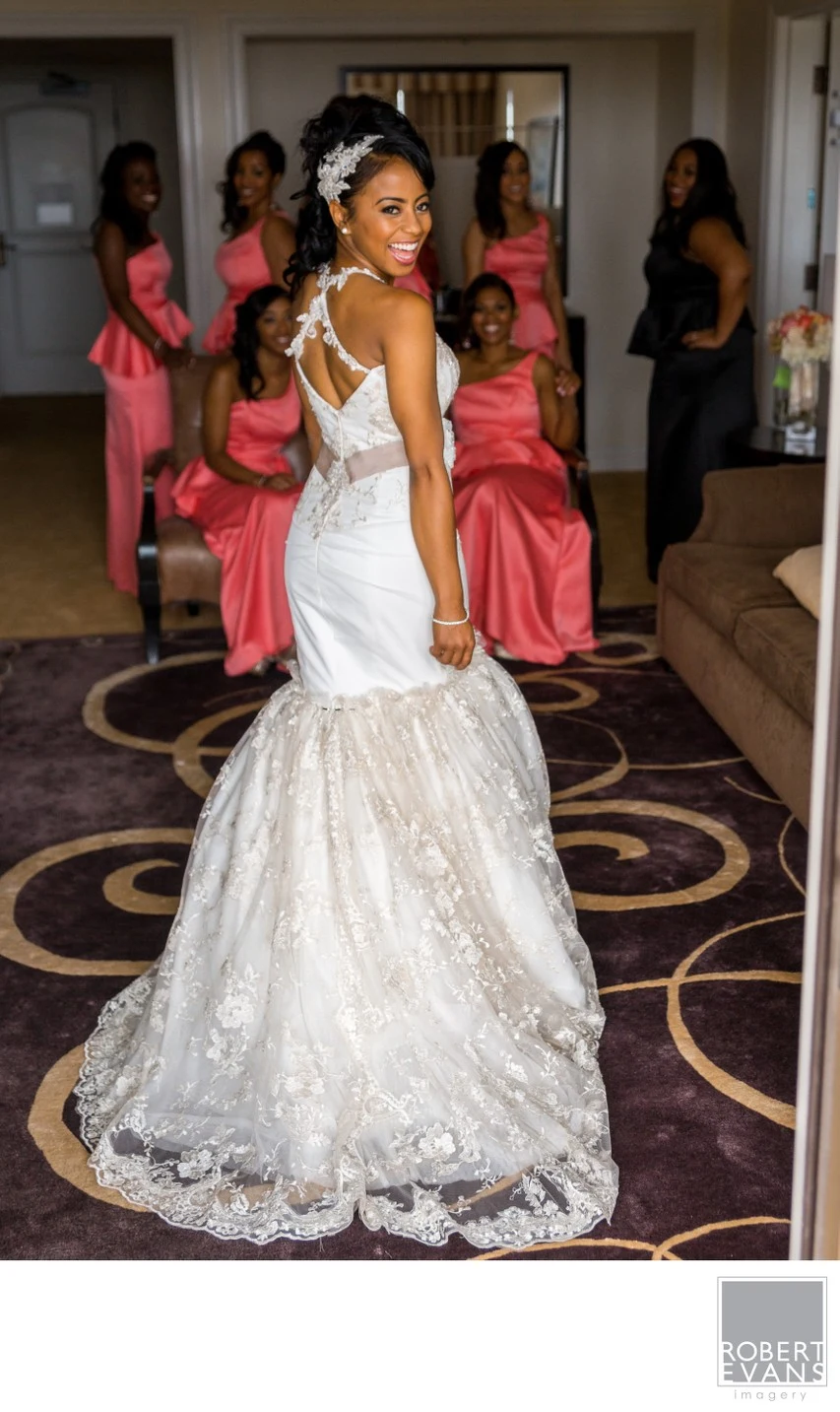 A bride turns toward smiling bridesmaids in bright dresses during wedding preparations.