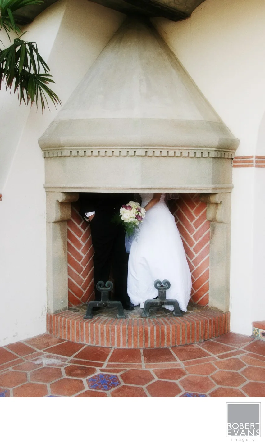 A wedding dress hangs inside a tall fireplace alcove above a tiled floor.