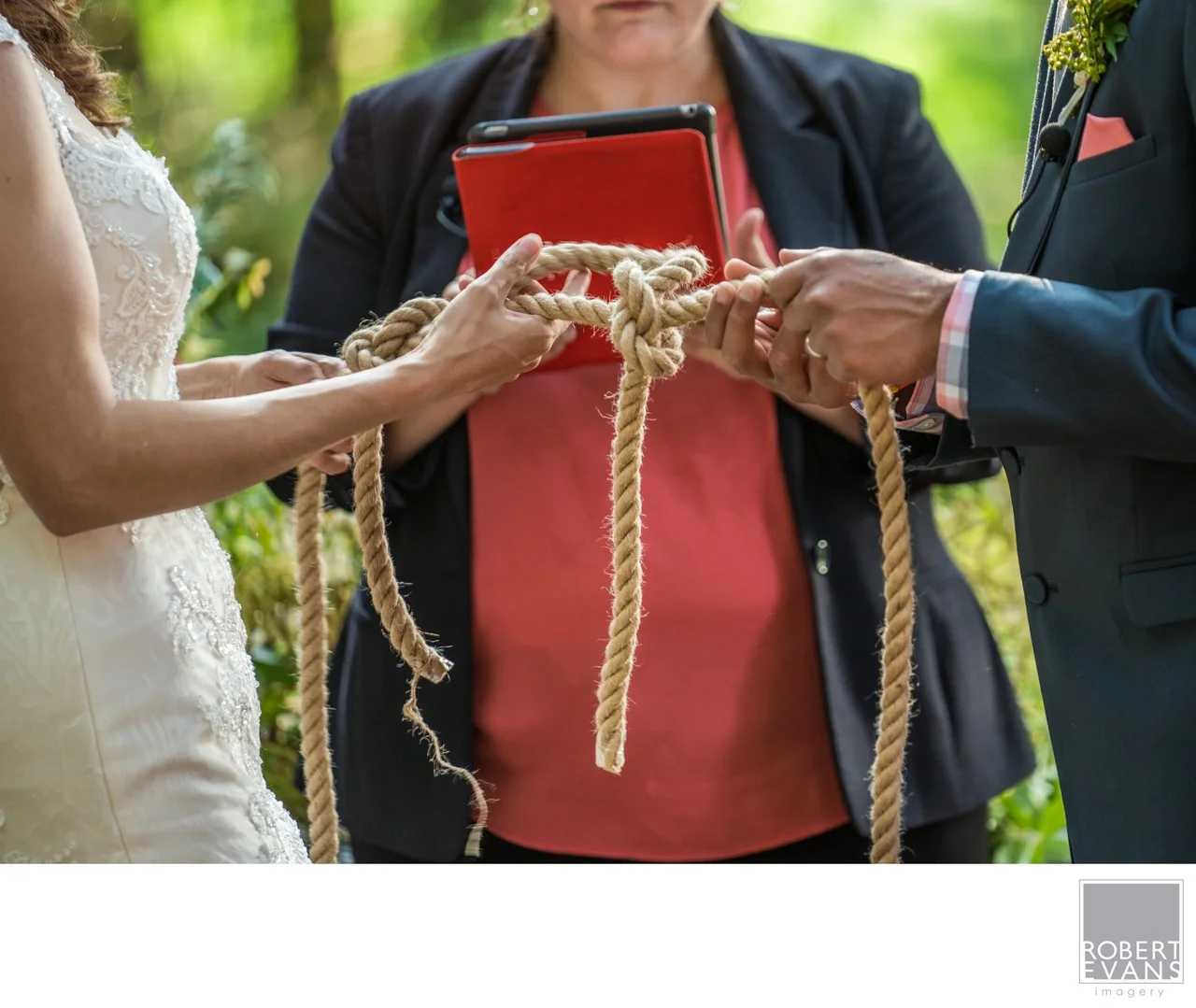 A couple’s hands hold a knotted rope during an outdoor wedding ceremony.