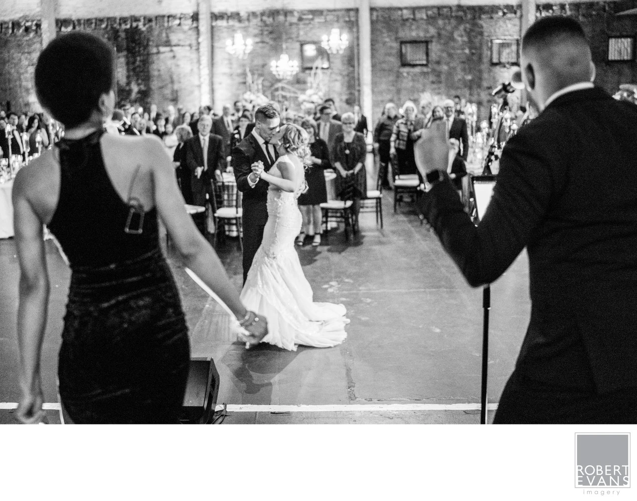 A bride dances while guests watch around her in a lively black-and-white reception photograph.