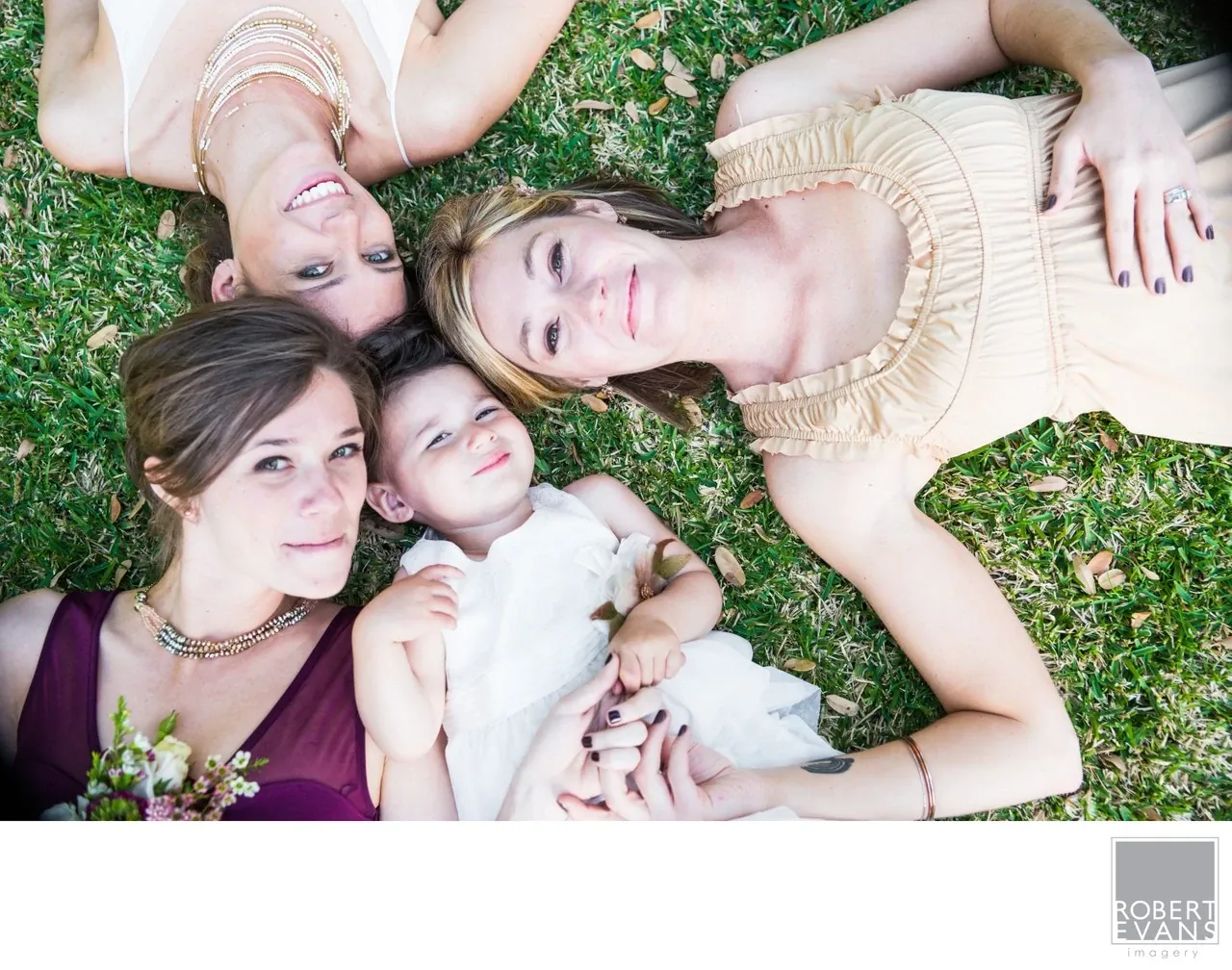 Three women and a child lie close together on green grass, photographed from above.
