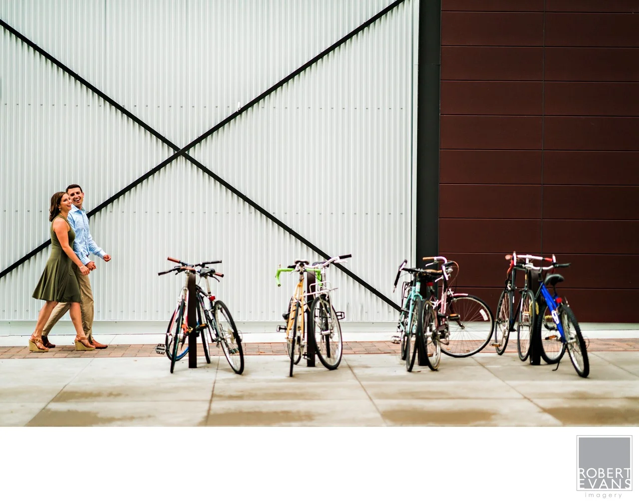 A couple walks beside parked bicycles and a large industrial wall.