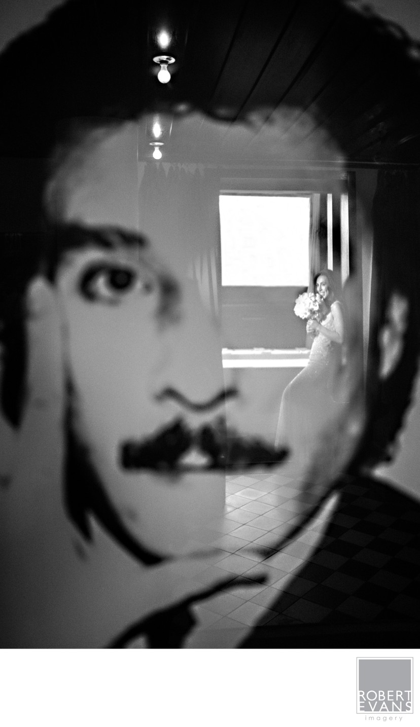 A large monochrome face on a wall overlaps reflections and a small figure in glass.