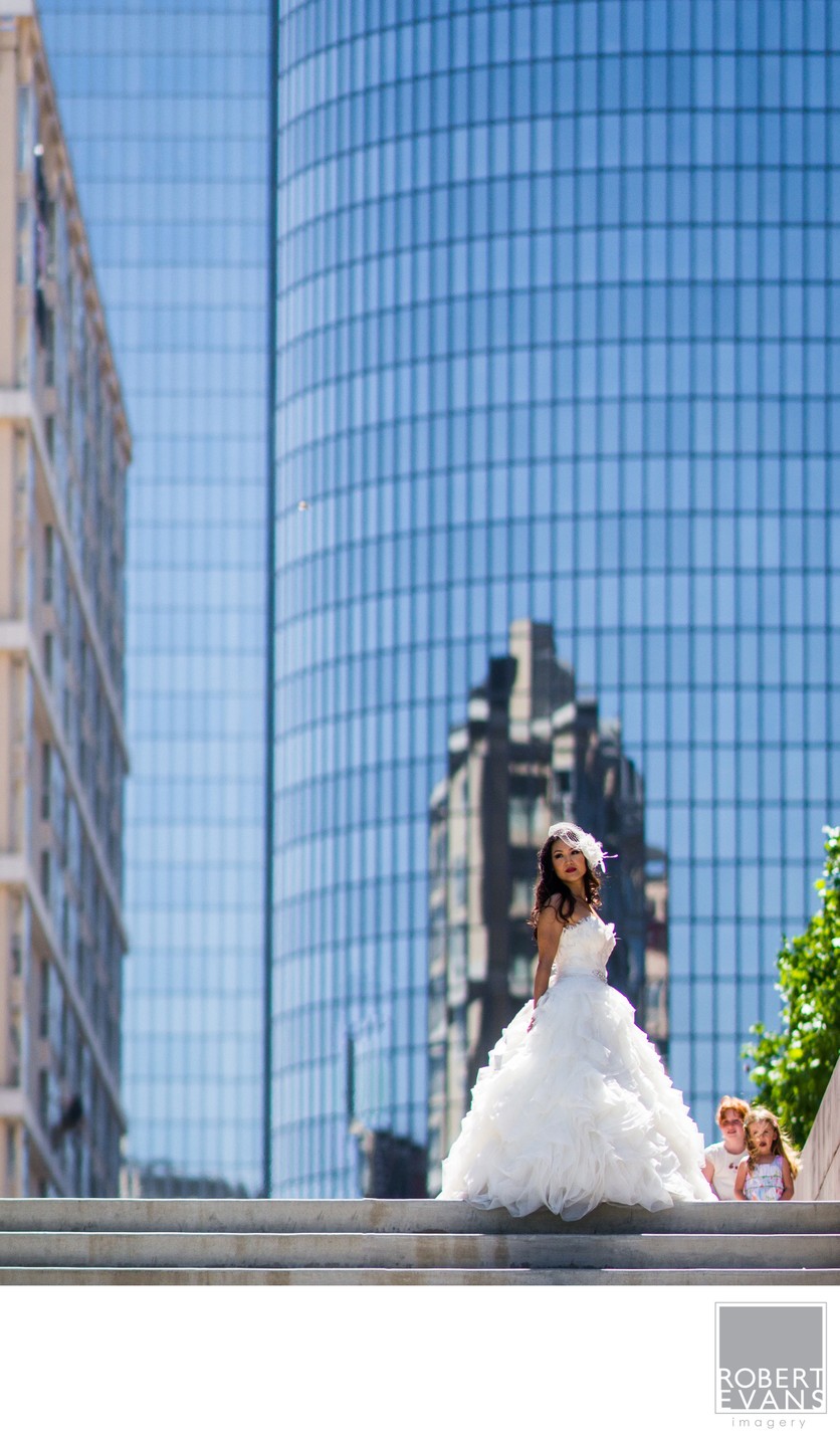 A bride and groom stand together beneath a tall reflective city building.