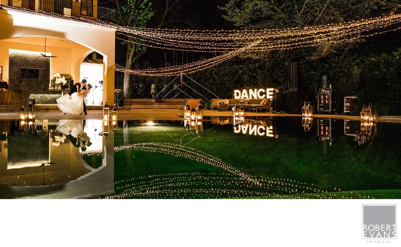 A wedding reception glows with string lights beside a pool reflecting the celebration.