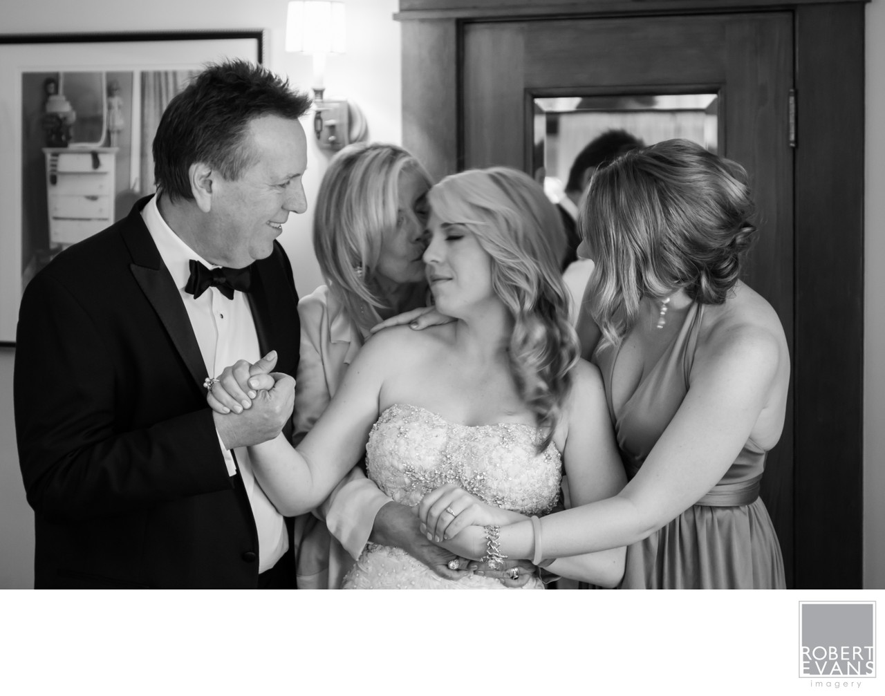 A bride laughs between her groom and a woman beside her in black and white.