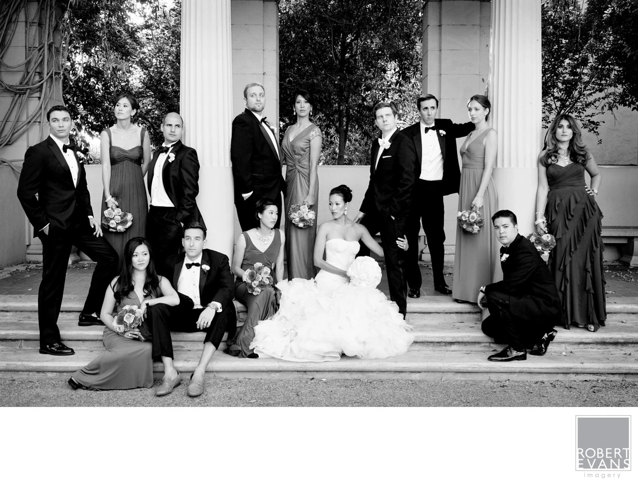 A wedding party poses across broad stone steps in a black-and-white group portrait.