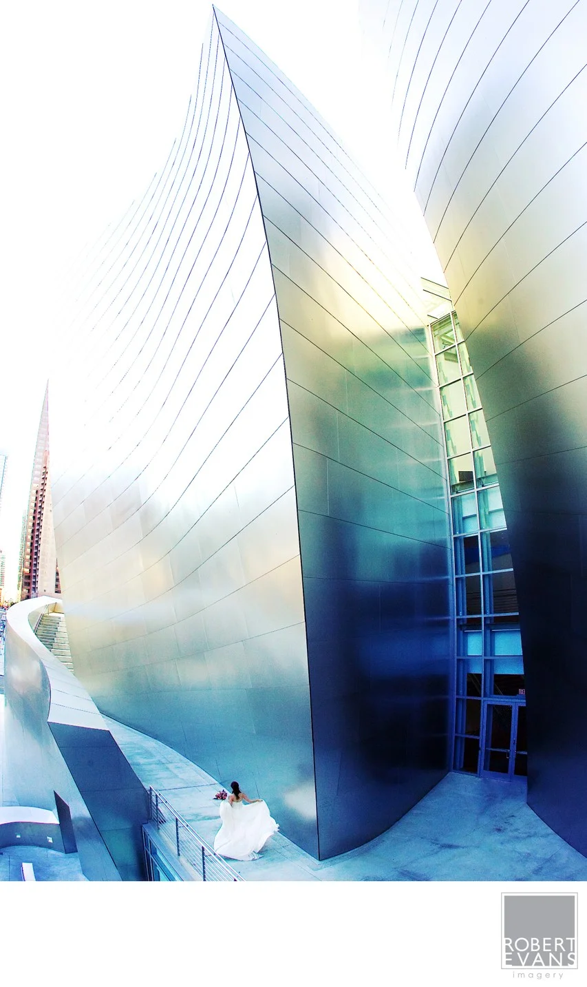 A small bridal figure stands below towering curved metallic walls catching blue and gold light.