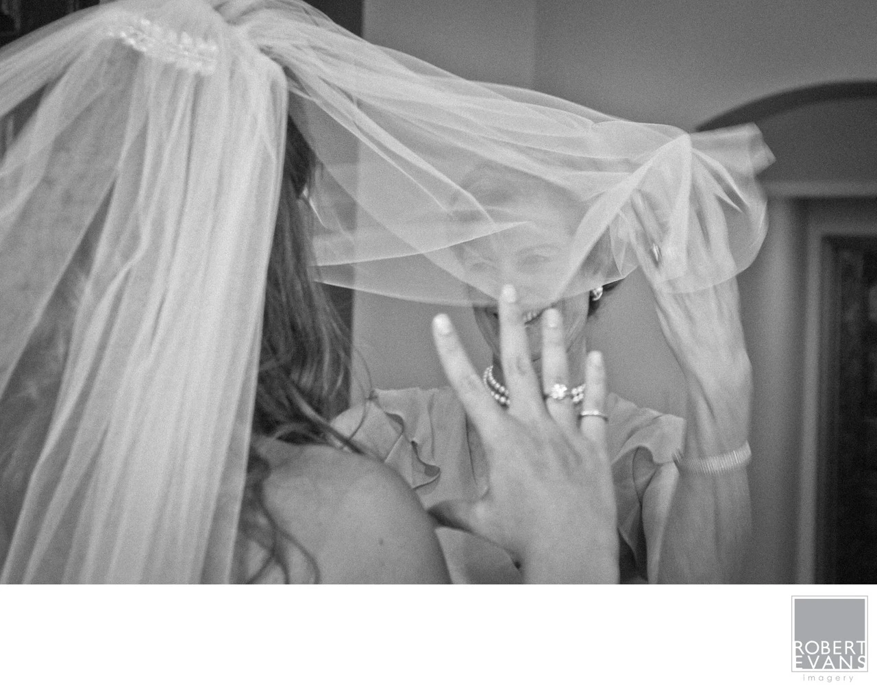 A bride and groom kiss beneath a sheer veil in a close black-and-white photograph.