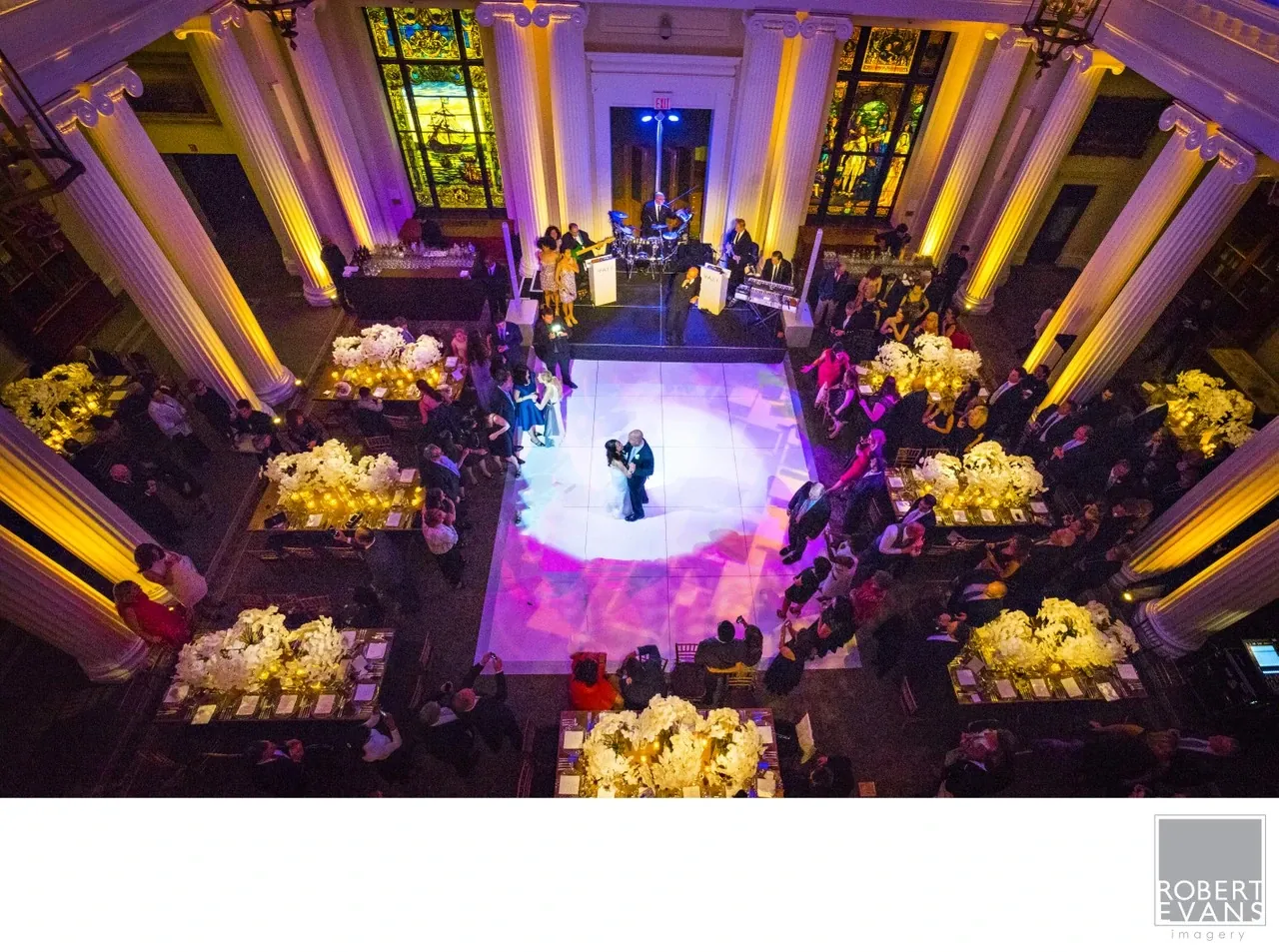 A couple dances at the center of an ornate reception hall lit in purple and gold.