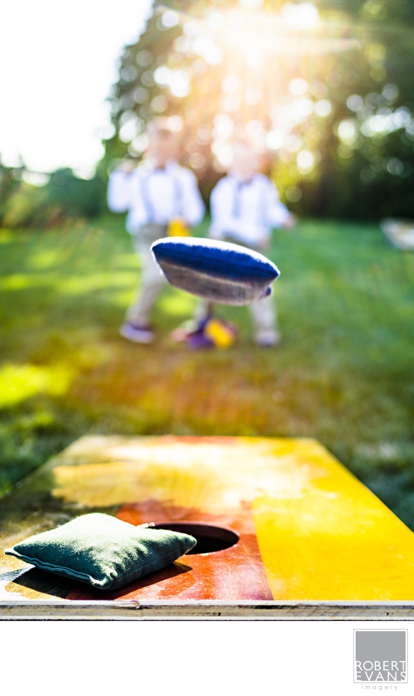 A colorful beanbag flies toward a game board on a sunlit lawn during a wedding celebration.