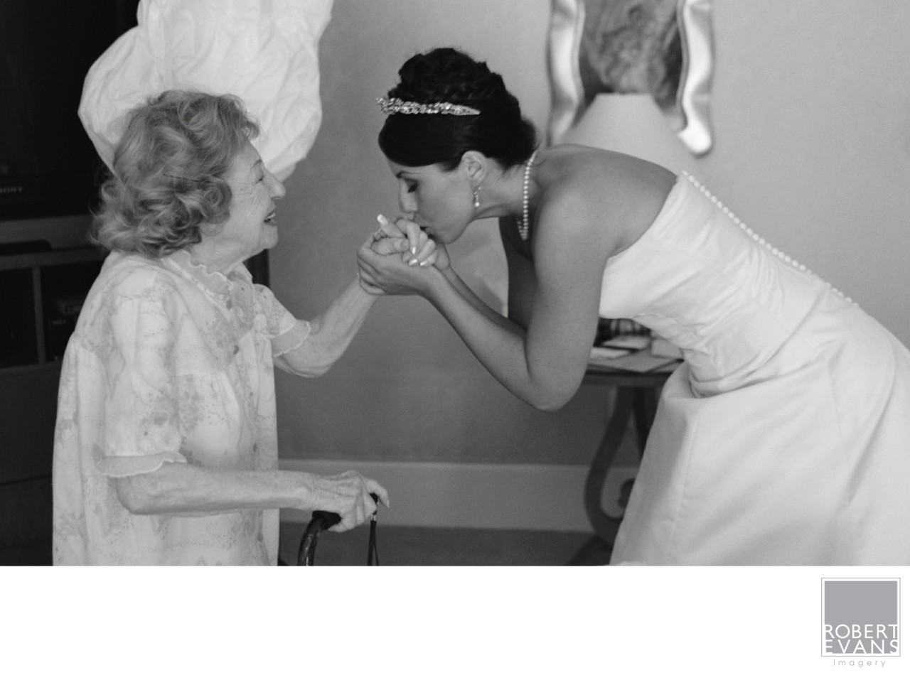 A bride bends to kiss an older woman’s hand during a tender black-and-white moment.