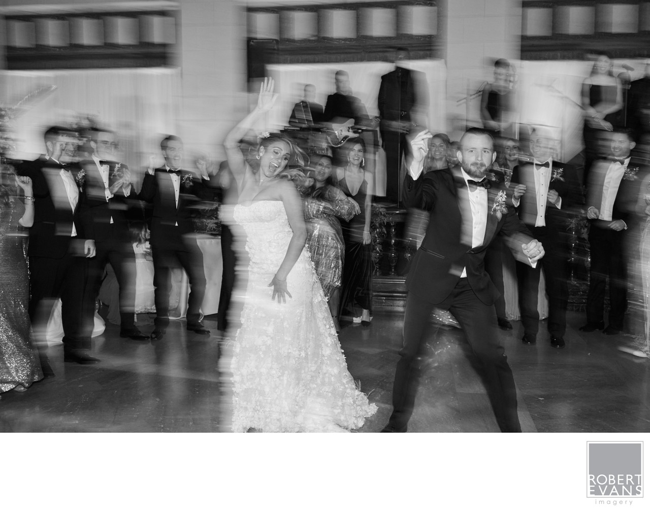 A bride and groom dance with motion blur as guests watch around them in black and white.
