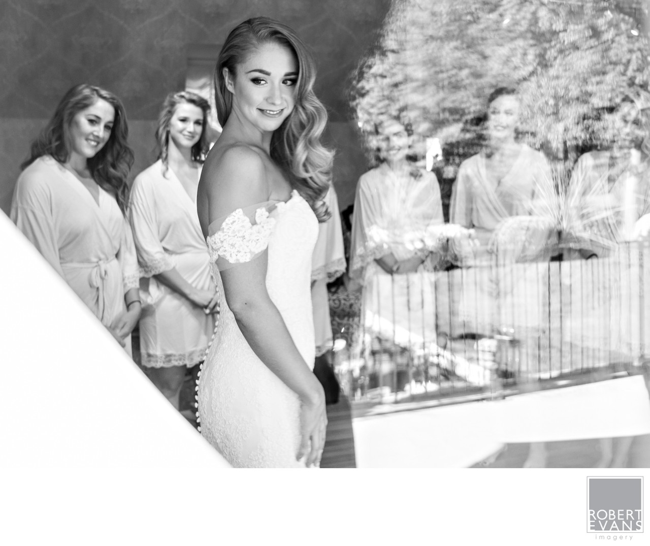 A bride and attendants appear through layered window reflections in black and white.