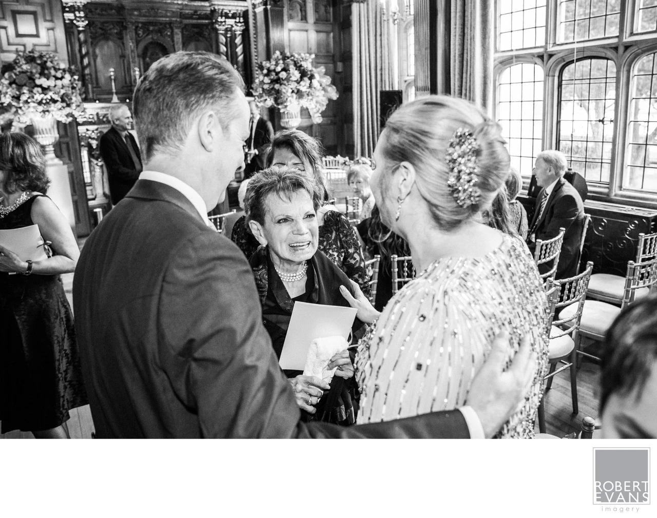 A bride and groom speak with an older woman during a wedding celebration in black and white.