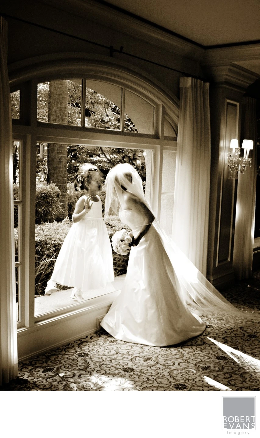 A bride stands before a large arched mirror in a softly lit room.