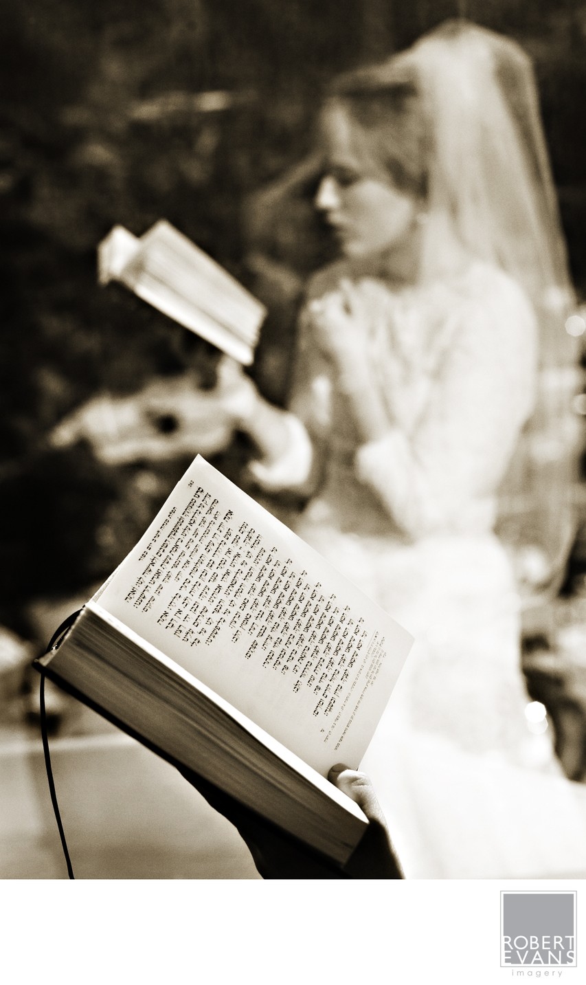 An open book fills the foreground while a veiled bride stands beyond it in soft focus.