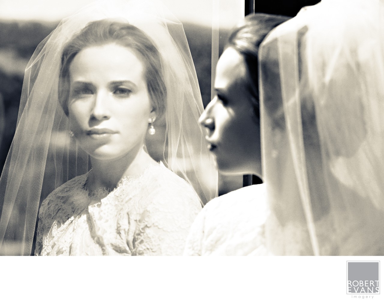 A close bridal portrait and reflection overlap beneath sheer veil fabric in monochrome.