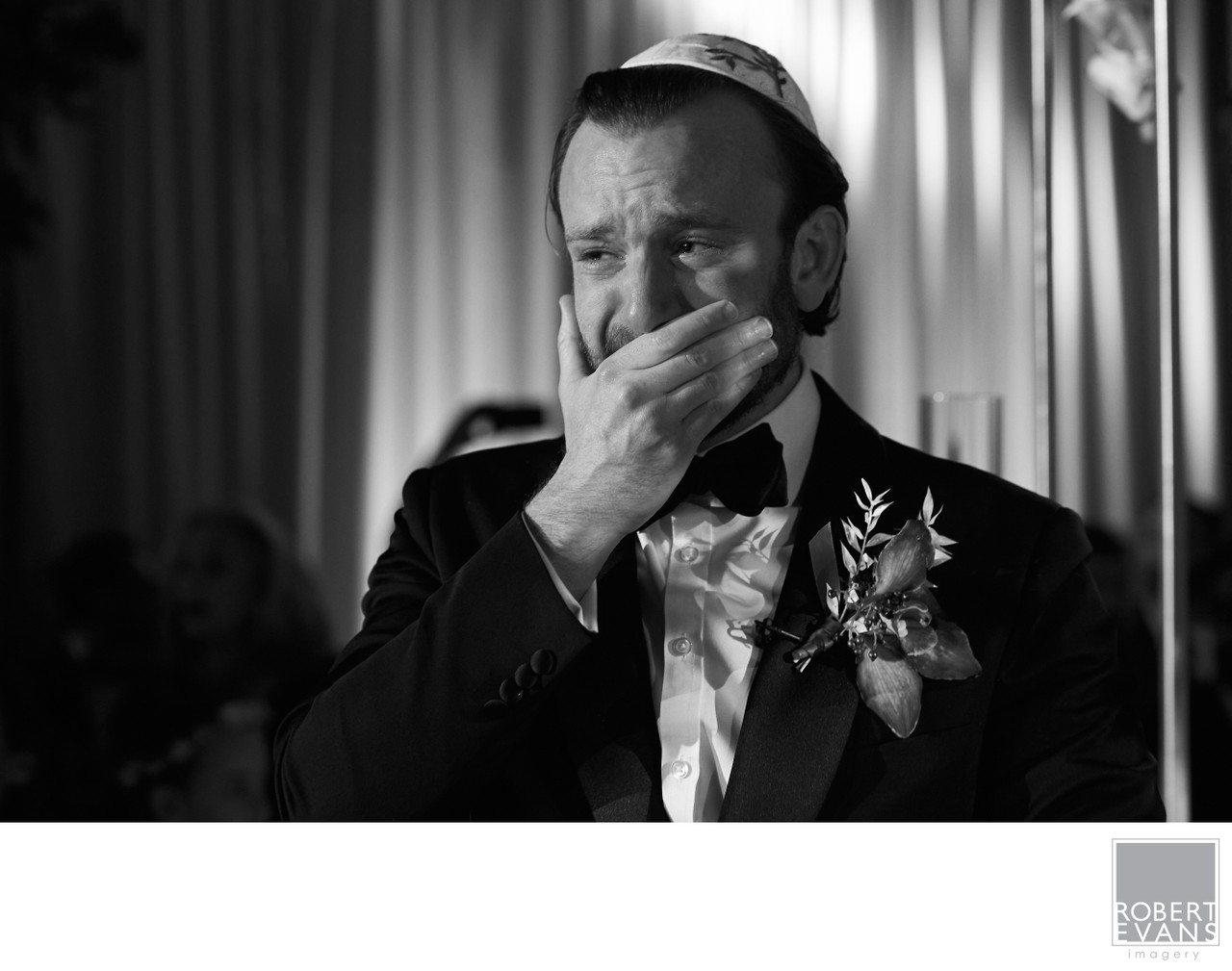A groom raises his hand to his mouth with an emotional expression in black and white.