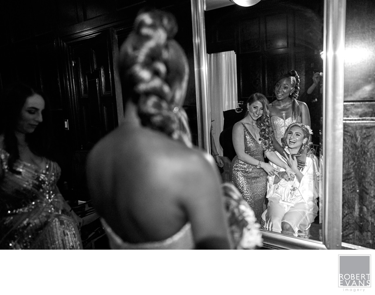 A woman’s braided hair fills the foreground while a bride and companions appear in a mirror.