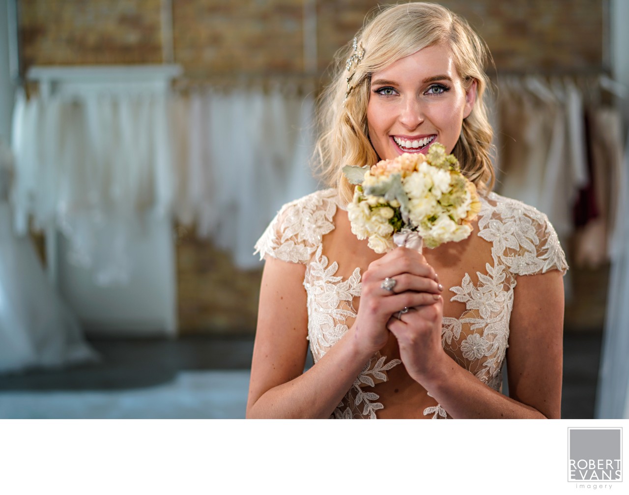 A smiling bride holds a small pale bouquet beneath her chin.